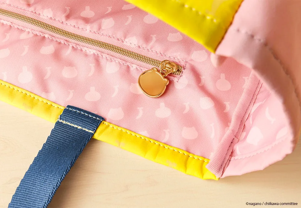ピンク色の裏地と黄色い縁取りが施された、ジッパー付きのトートバッグ。ジッパーにはクマの形のチャームが付いており、持ち手は青色である。
