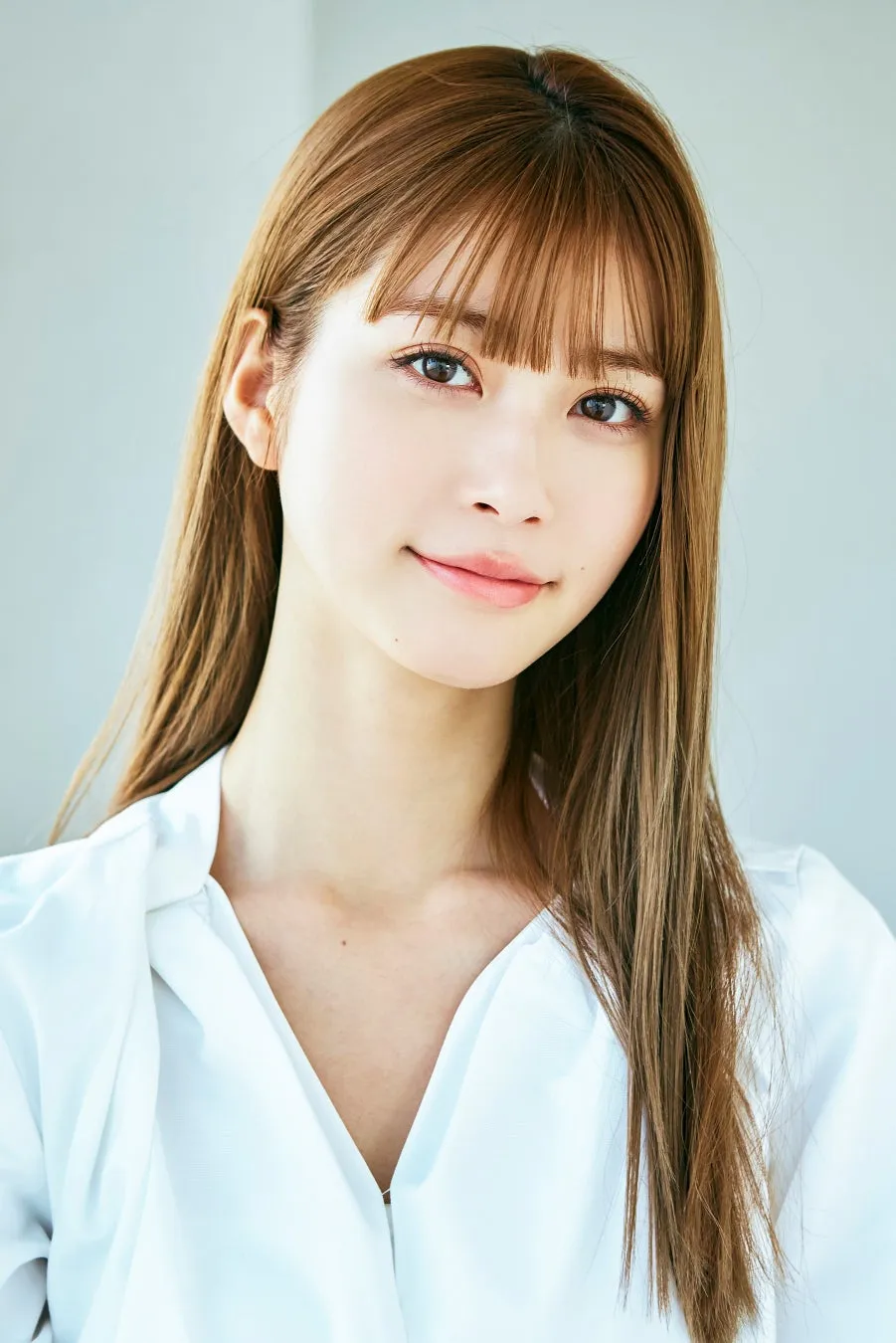 女性のポートレート。長い茶色の髪で、白いシャツを着ています。背景は明るい。