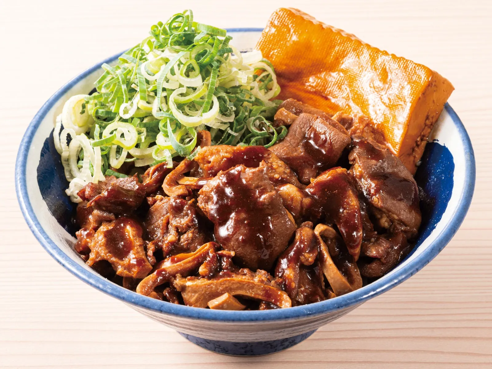 丼に入った料理の写真。茶色い煮込み肉とネギ、揚げ豆腐のようなものが盛られている。料理には甘辛いソースがかかっている。
