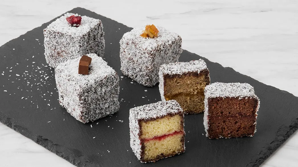 2つのランミントンケーキが並んでおり、1つは半分にカットされています。ケーキはココナッツで覆われており、表面には何かトッピングがされています。