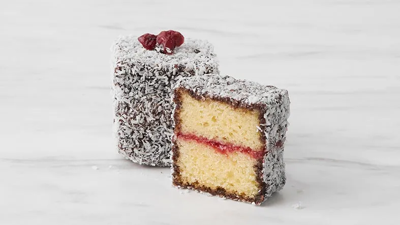 2つのラミントンケーキ、1つは半分にカットされ、ラズベリージャムが詰められています。ココナッツフレークで覆われています。