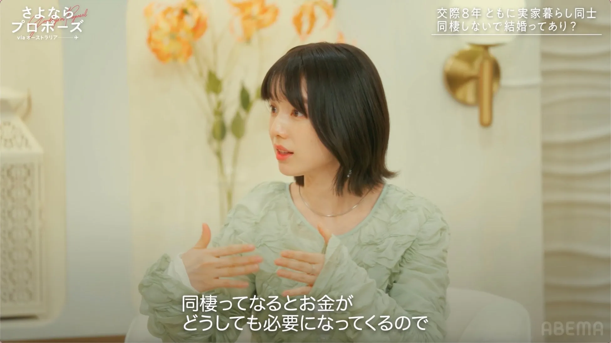女性がインタビューを受けている様子。背景には花が飾られており、番組のロゴとテキストが表示されている。