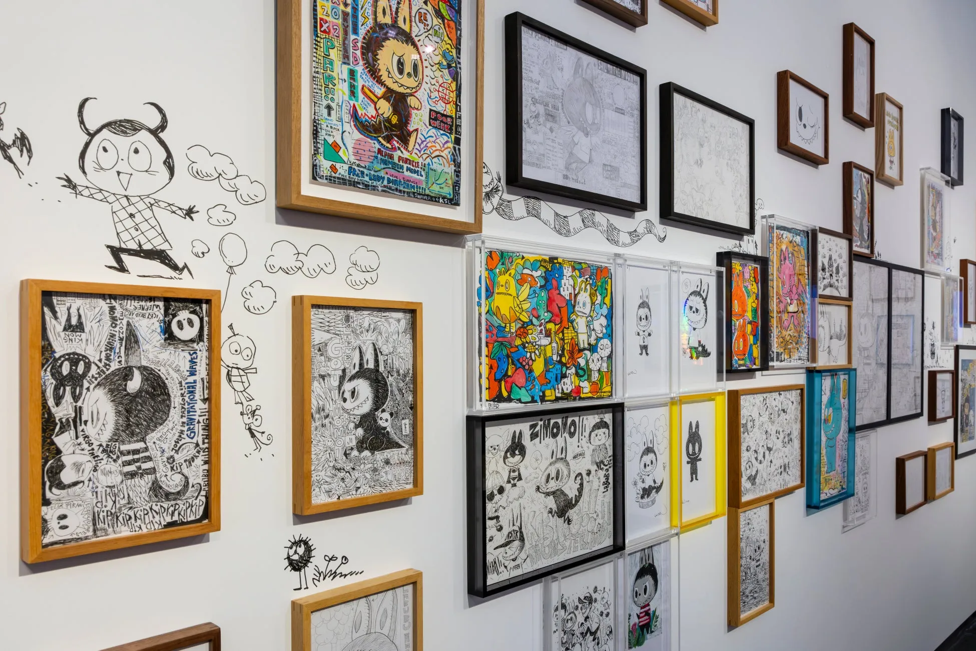 白い壁に飾られた、様々なフレームに入った手描きのイラストの展示