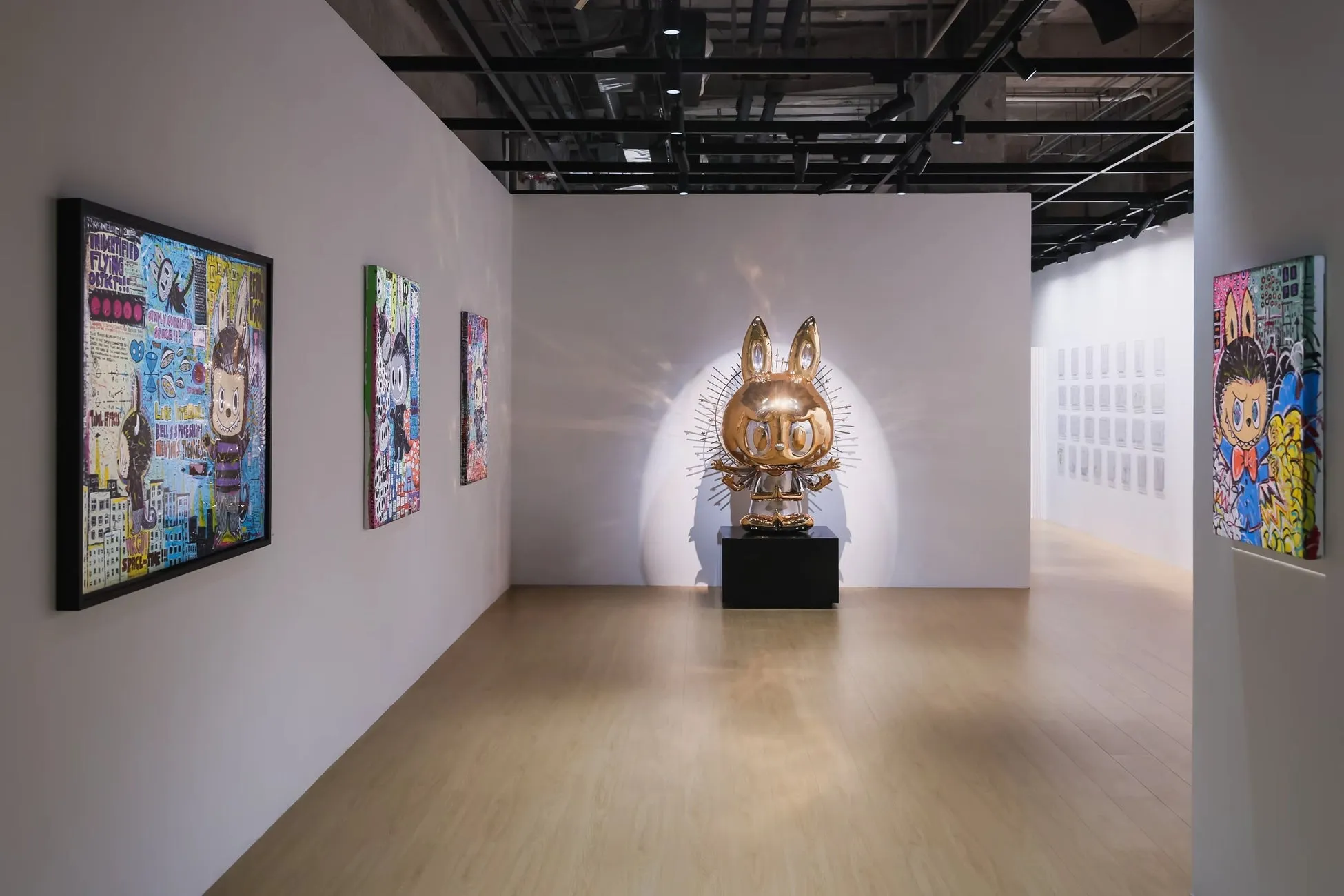 現代アートの展示室内の様子。金色のウサギの彫刻が中央に配置され、壁にはカラフルな絵画が飾られています。