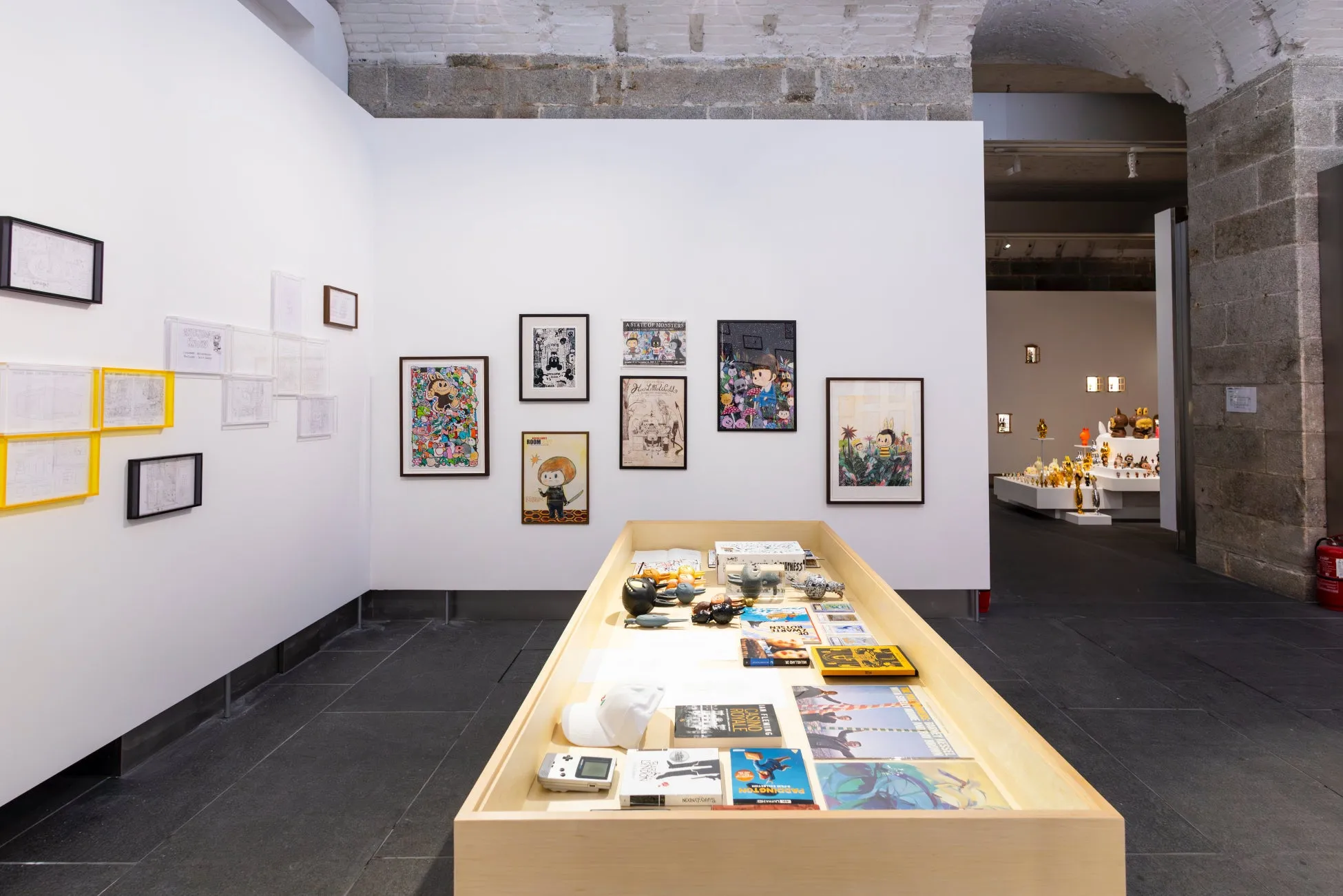 ギャラリーの展示。壁にはフレームに入ったアート作品が飾られており、中央には展示品が並べられたテーブルがある。