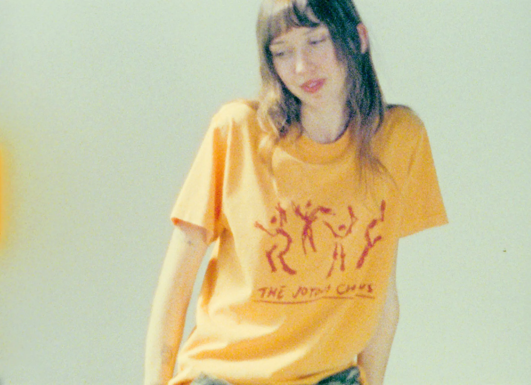 女性がオレンジ色のTシャツを着ていて、そのTシャツにはイラストと文字がプリントされています。