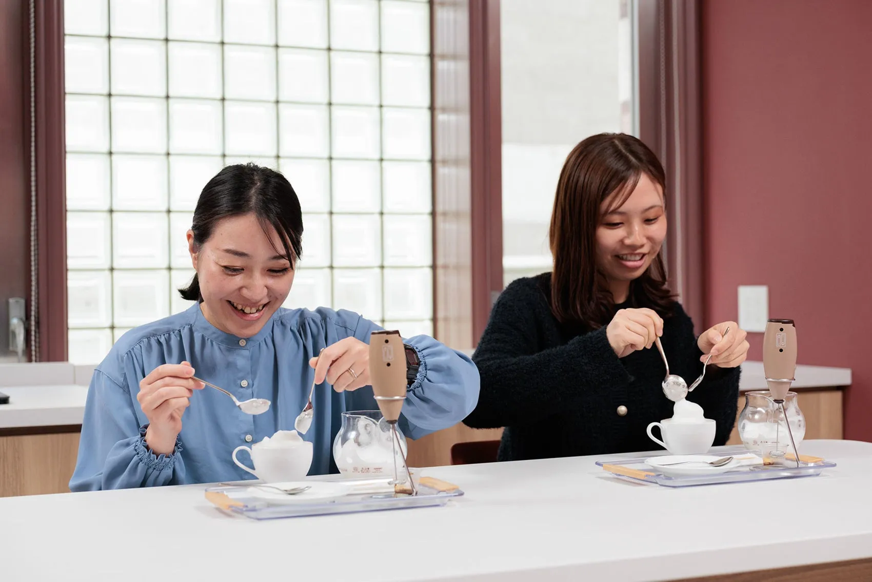 2人の女性が、テーブルで泡立て器を使って飲み物にクリームを乗せている様子。