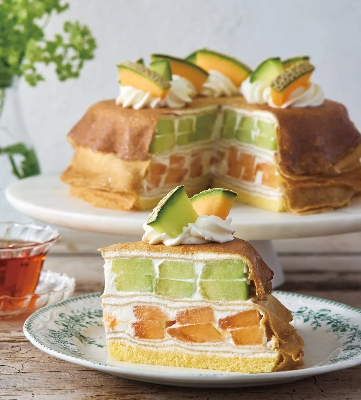 メロンがたっぷり使われたケーキの画像です。緑色のメロンとオレンジ色のメロンが交互に層になっており、クリームで飾られています。ケーキの上にはメロンのスライスがトッピングされ、見た目にも美しいデザートです。