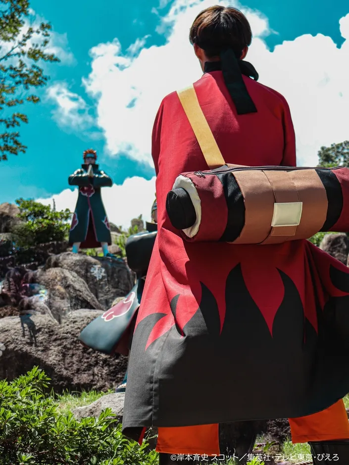 NARUTOのキャラクターのコスプレをした人が、NARUTOの像を背景に立っている写真