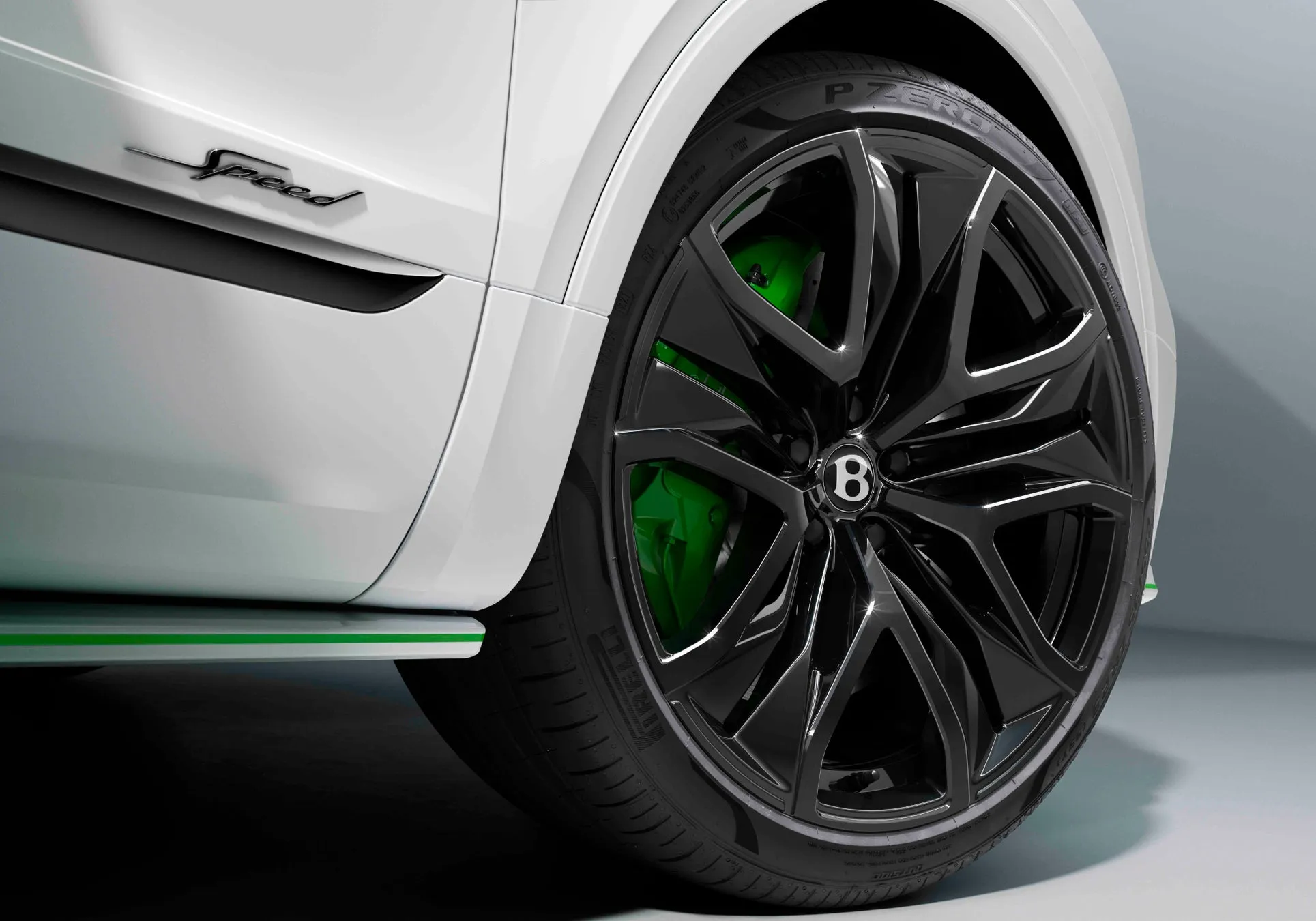 白の車の一部のクローズアップ。黒いホイールと緑色のブレーキキャリパーが特徴。