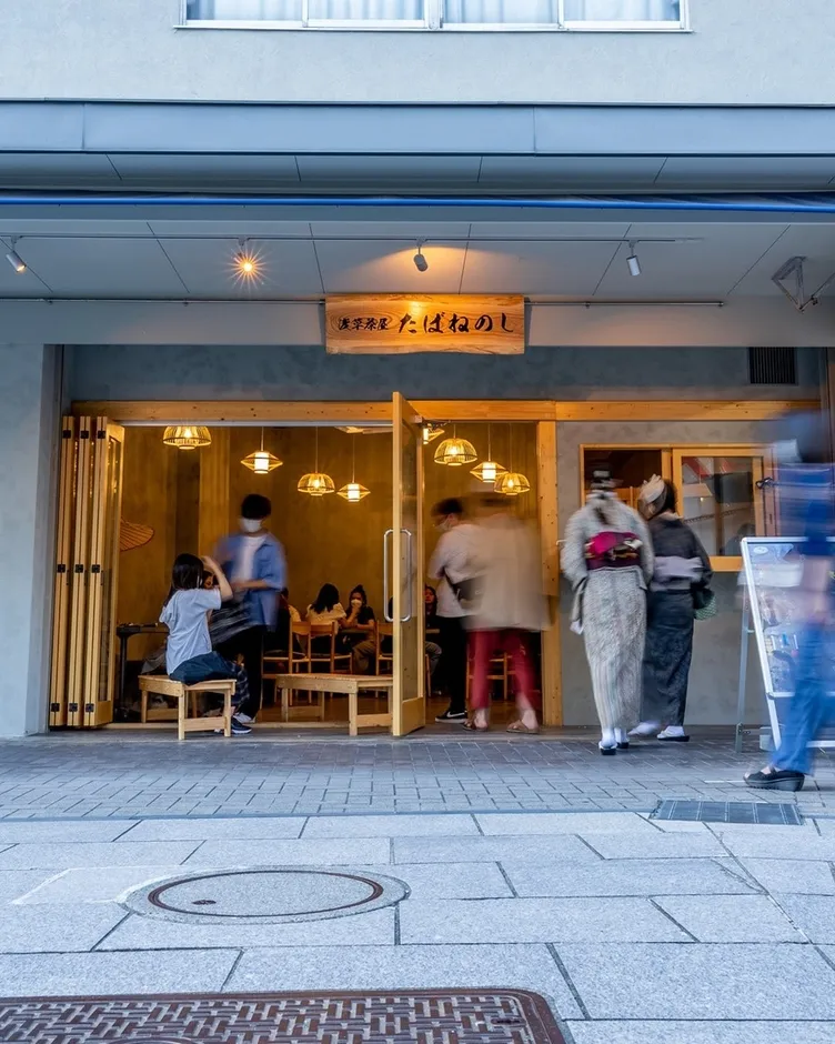お店の入り口に立っている人々と、着物を着た女性たちが写っている写真です。お店の看板には「濃厚茶屋 たばねのし」と書かれています。