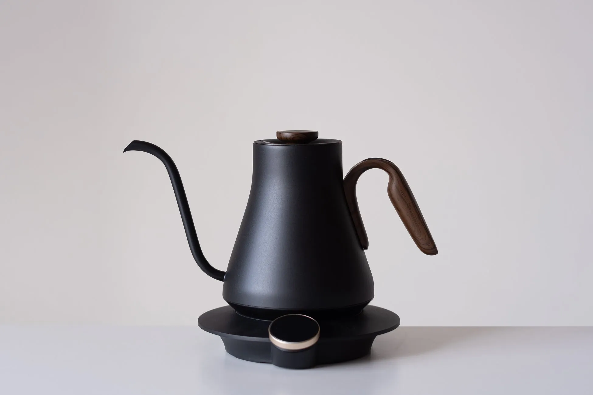 黒い電気ケトルのクローズアップ写真。木製のハンドルと蓋が付いており、白い背景に置かれています。