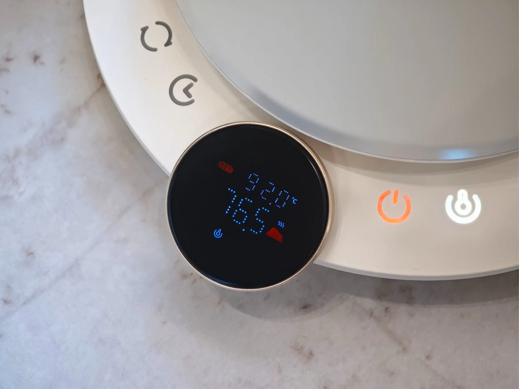 丸いディスプレイを持つ白い家電製品。ディスプレイには温度が表示され、電源ボタンとその他のコントロールが表示されています。