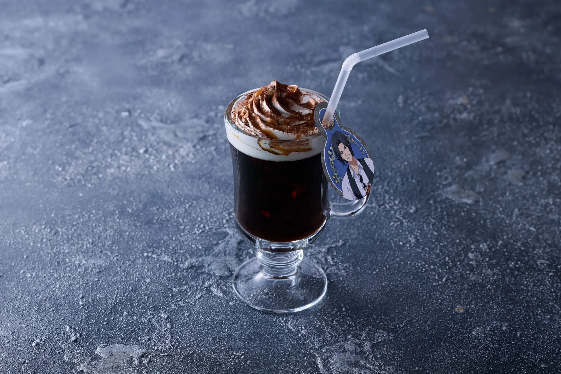 ホイップクリームとチョコレートパウダーがトッピングされた、グラスに入ったコーヒー。ストローとキャラクターの装飾が付いています。