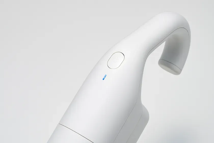 白い掃除機のクローズアップ画像。電源ボタンと青いインジケーターライトが確認できる。