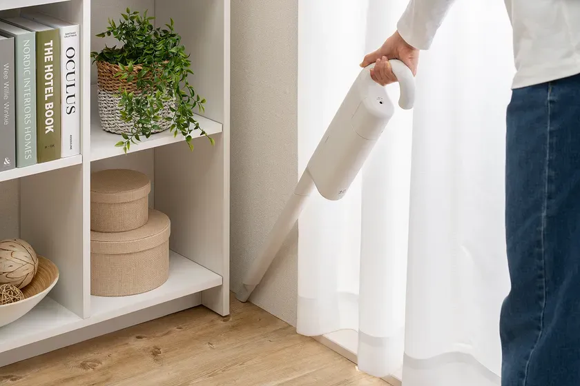 掃除機で掃除をしている様子。棚には本や植物、丸い箱が置かれている。