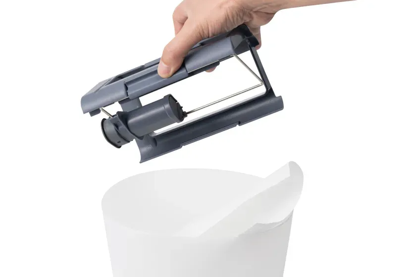 手で持たれた灰色の部品が、白い容器の上に置かれようとしている様子を描いた画像です。