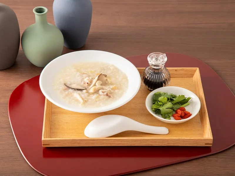 白い器に入ったお粥が写っている。薬味と醤油も添えられており、食卓を彩る様子が写っている。