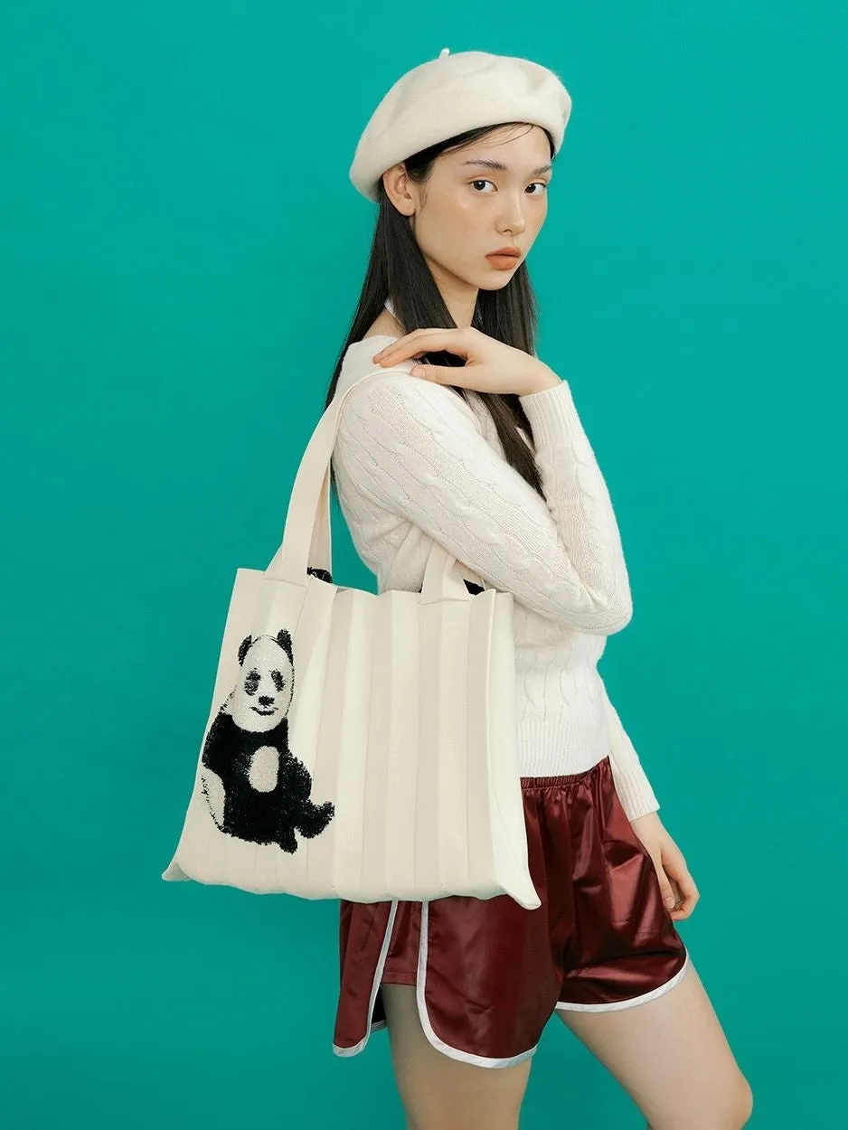 女性が白いベレー帽とセーターを着て、パンダの絵が描かれたトートバッグを持っています。