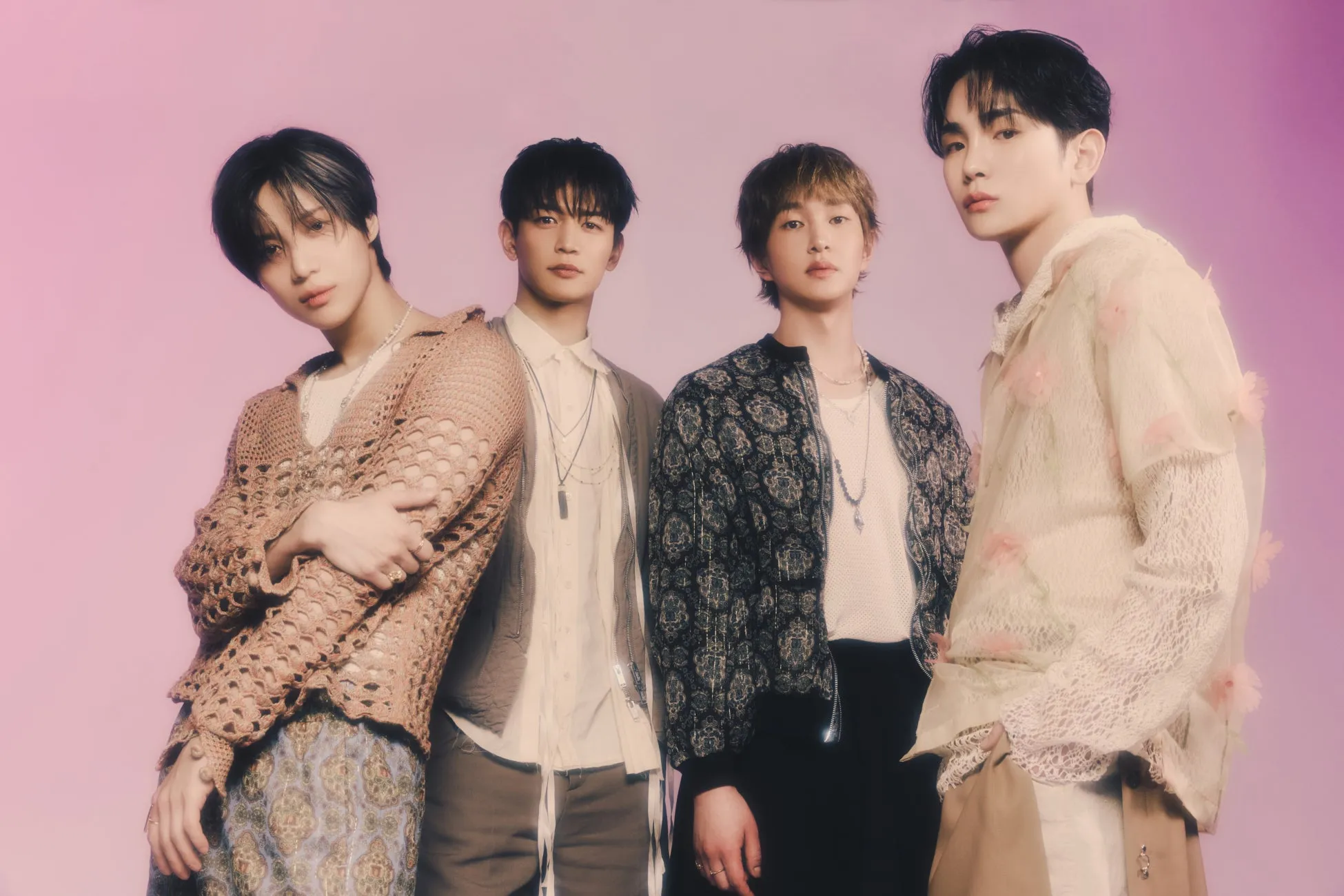 4人の男性がピンク色の背景の前に立ってポーズをとっている写真です。彼らは皆、さまざまなファッションの服を着ています。