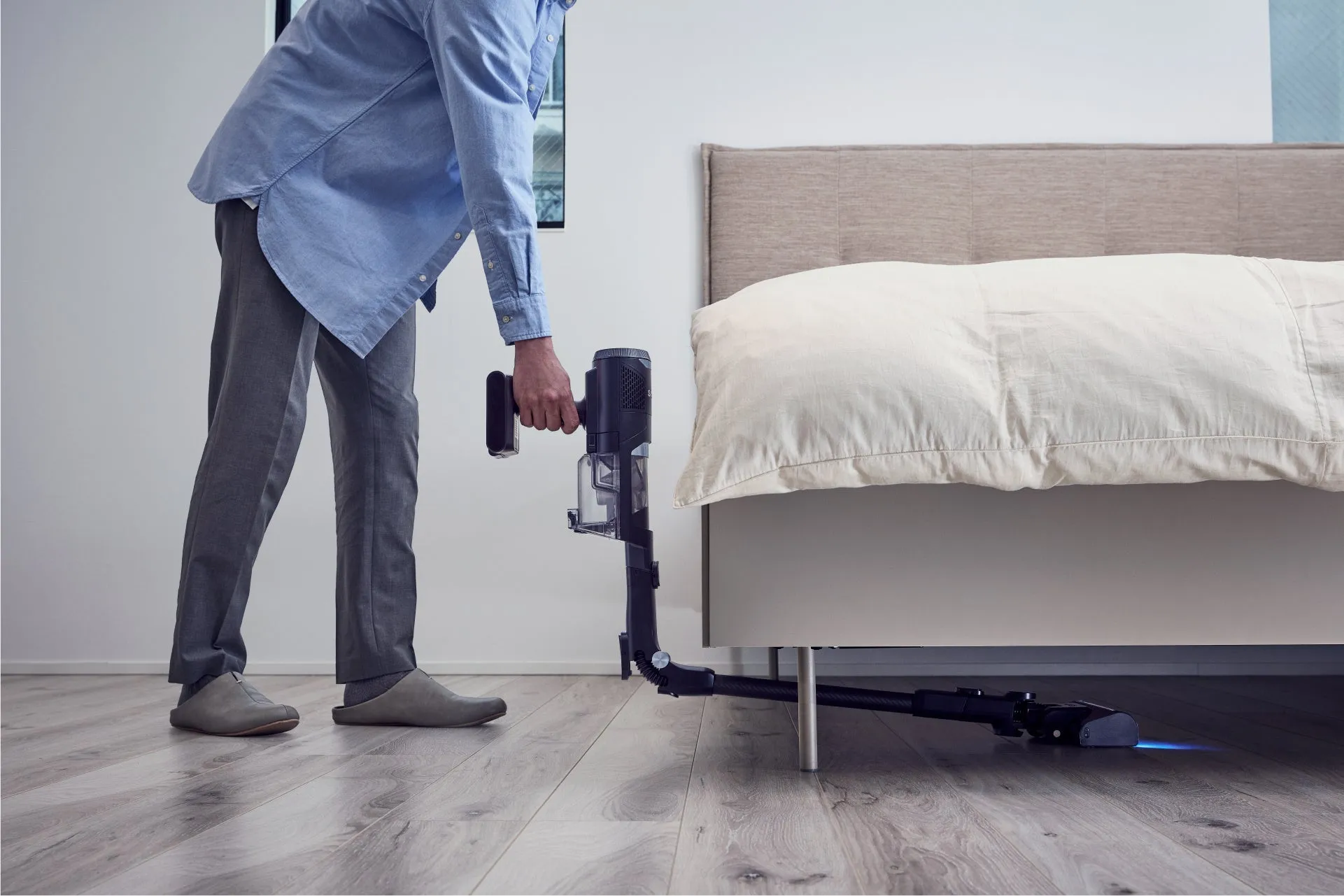 男性が掃除機を使ってベッドの下を掃除している様子。