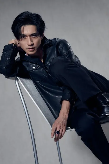 黒いスーツを着た男性が椅子に座ってポーズをとっている写真