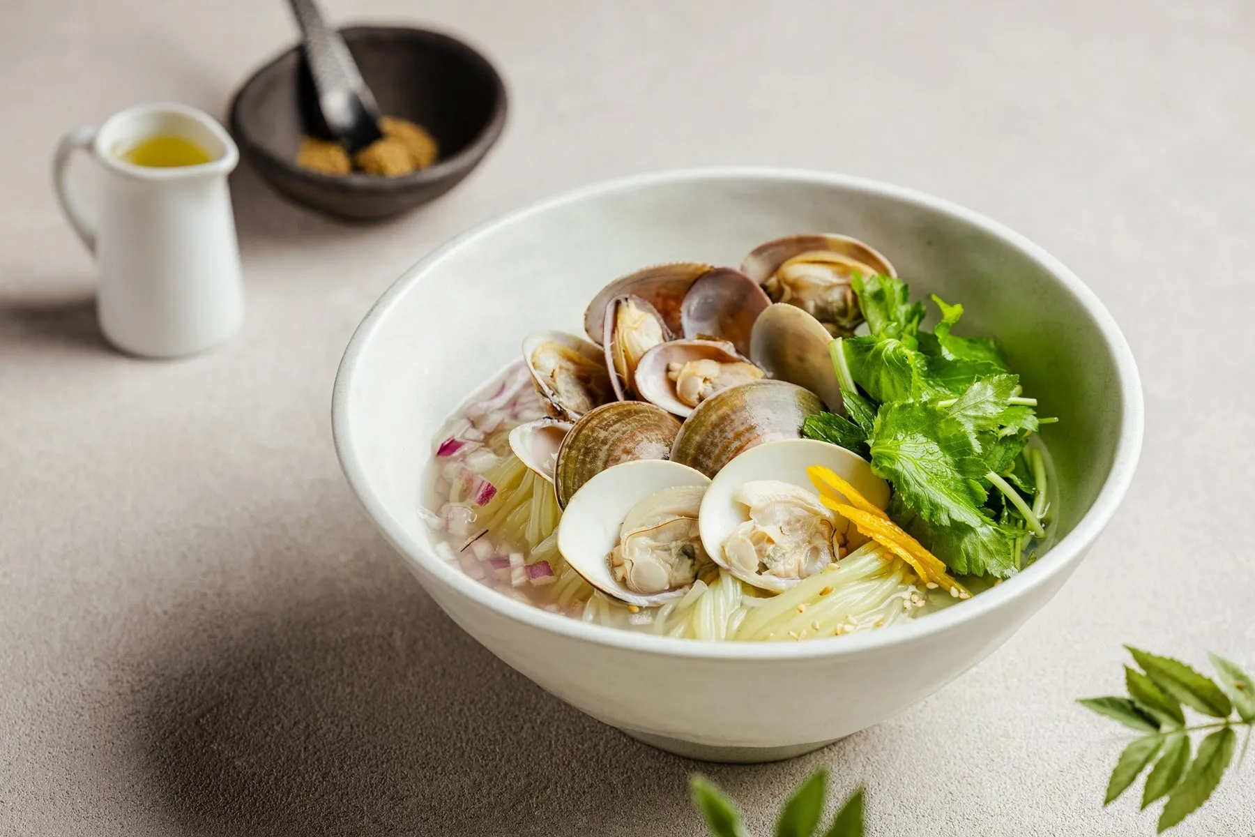 アサリと麺が入ったスープ。薬味と液体が入った容器も写っている。