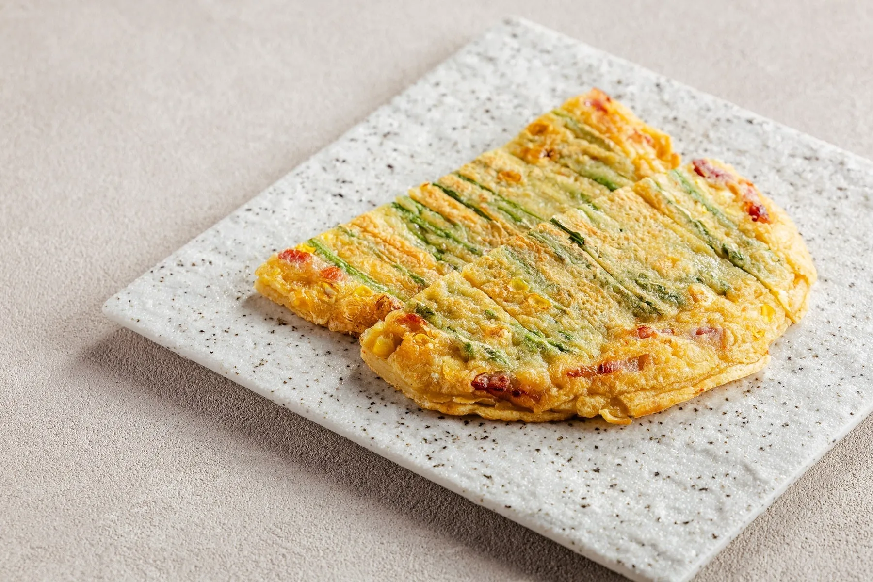 白いお皿に載せられた、ネギや野菜が練り込まれた韓国風チヂミのクローズアップ写真です。