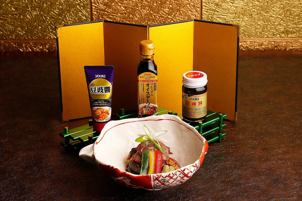 料理と調味料の配置写真。手前には料理が盛られた器があり、奥には調味料が並んでいる。背景には金色の屏風のようなものが配置されている。
