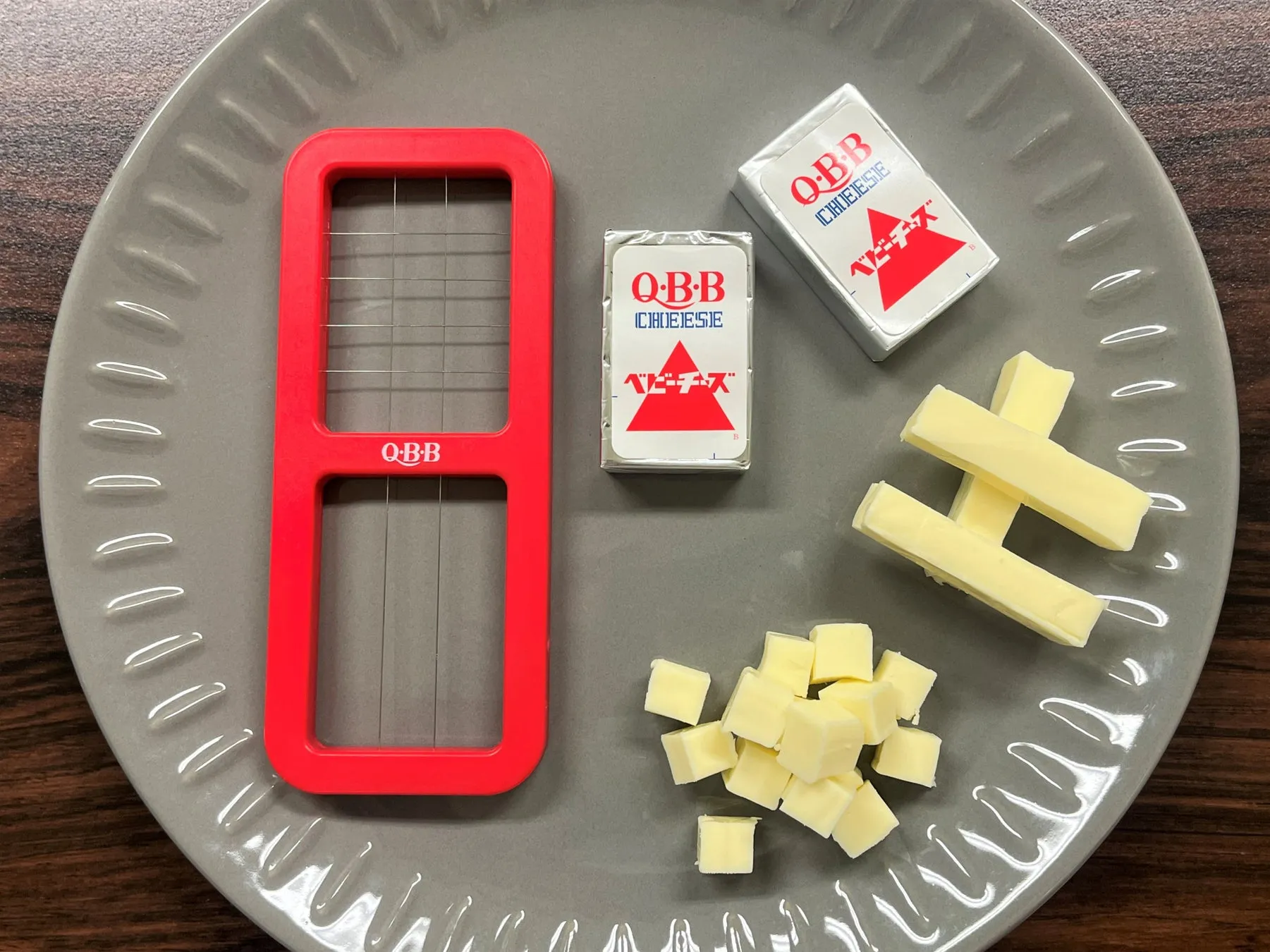 チーズ、チーズカッター、カットされたチーズ、およびチーズのパッケージがグレーの皿の上に置かれています。