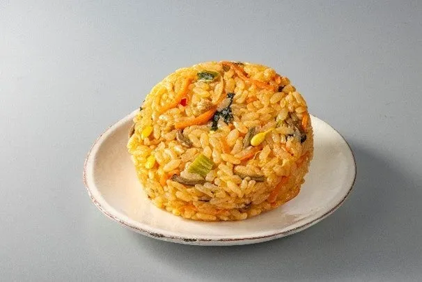 丸い形をしたご飯が白いお皿に乗せられています。ご飯には、野菜が混ぜ込まれています。