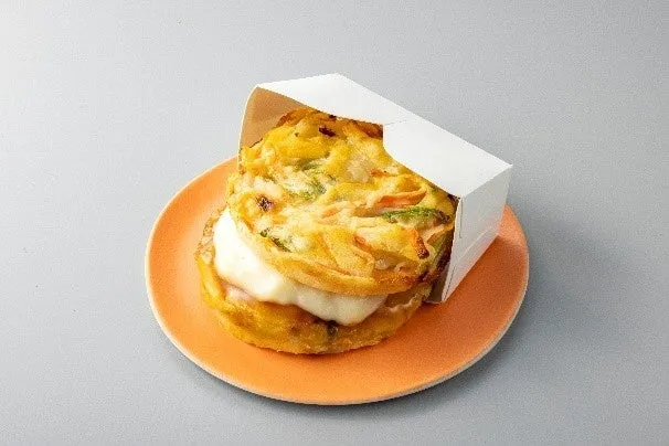 オレンジ色のお皿の上に、白い箱に入った食べ物があります。サンドイッチのように見えます。