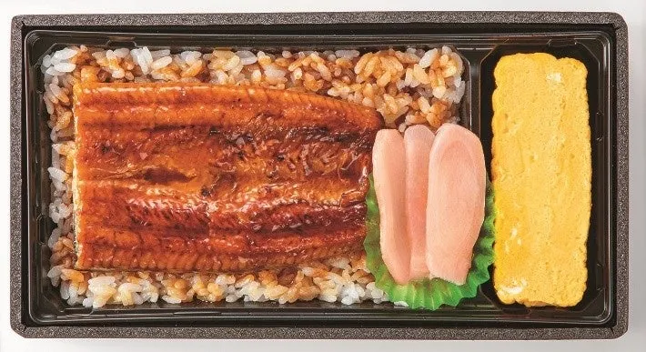 うなぎ弁当の写真です。ご飯の上にうなぎが乗っており、卵焼きと漬物も添えられています。