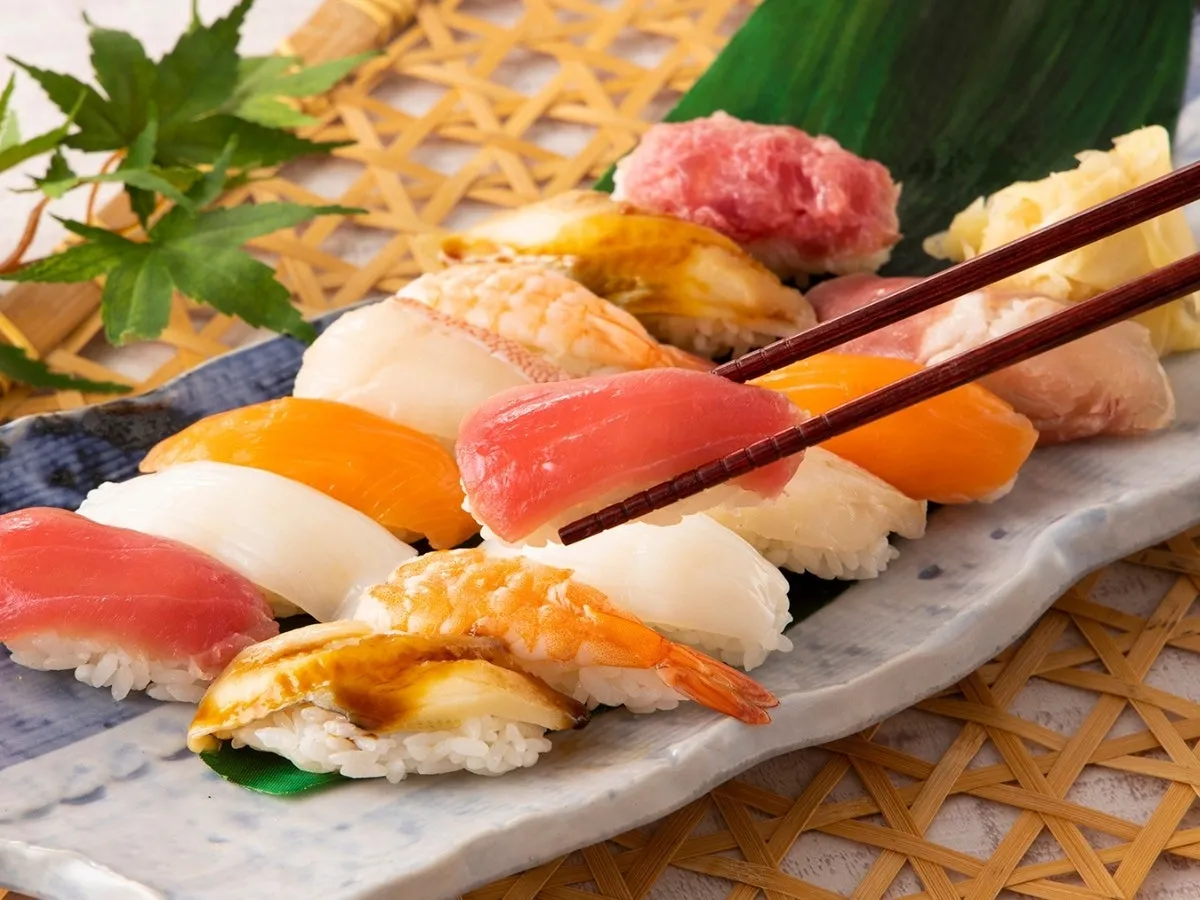 寿司の盛り合わせで、箸でマグロの握り寿司をつまんでいる様子。