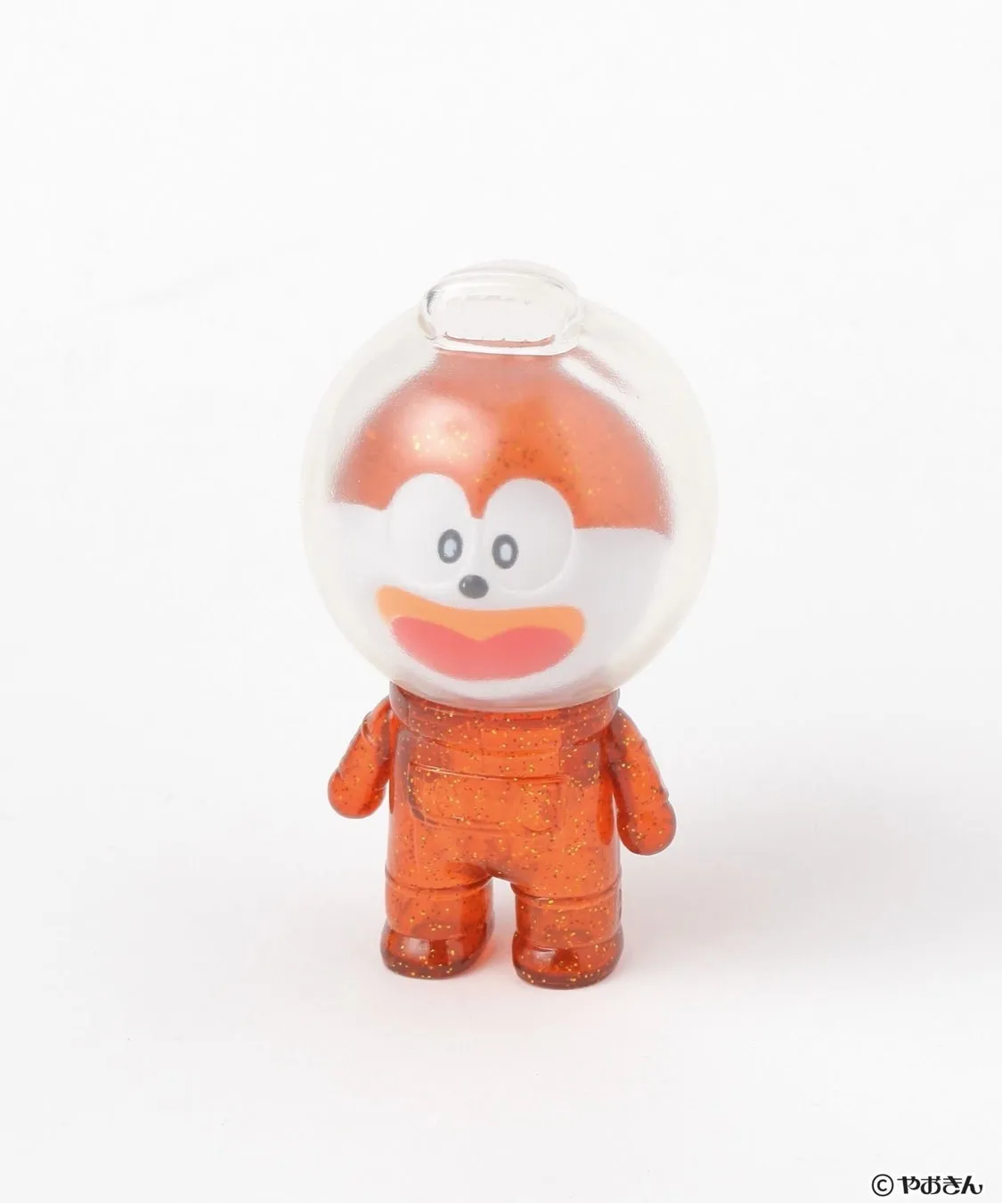 オレンジ色の宇宙服を着たキャラクターのフィギュア。頭部は透明なヘルメットで覆われ、顔は白とオレンジ色で、黒い目と赤い口が特徴的です。フィギュア全体にキラキラとした装飾が施されています。