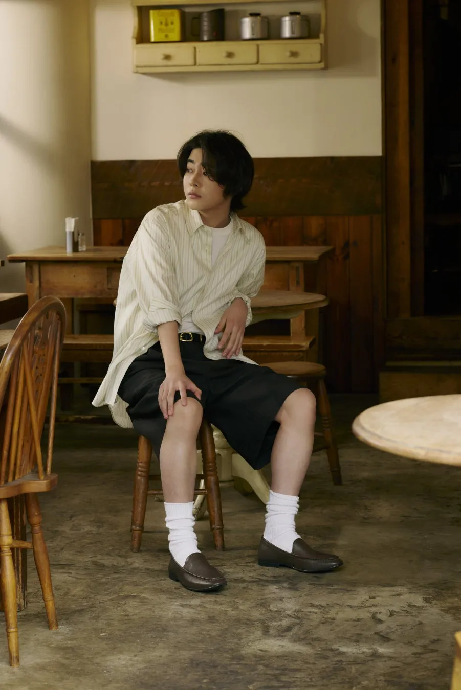 カフェのような場所に座っている男性のファッションポートレート。茶色のローファーを着用。
