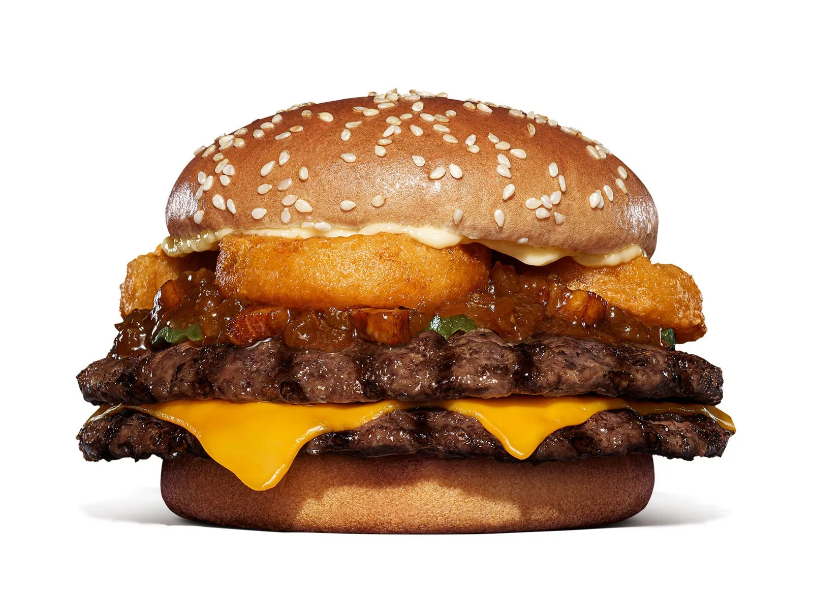 ハンバーガーのクローズアップ写真。白い背景に配置され、2つのパティ、チーズ、オニオンリング、ソース、ゴマ付きのバンズが特徴です。