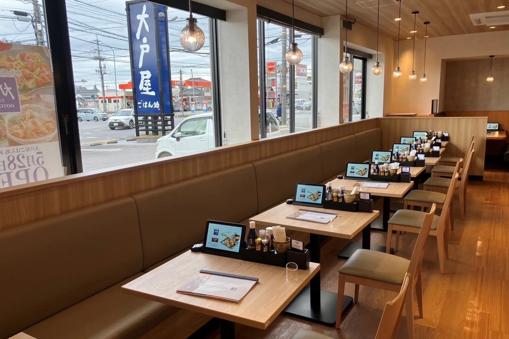 大戸屋の店内の様子。窓際の席が並び、各テーブルにはタブレットが設置されている。窓の外には車が行き交う様子が見える。