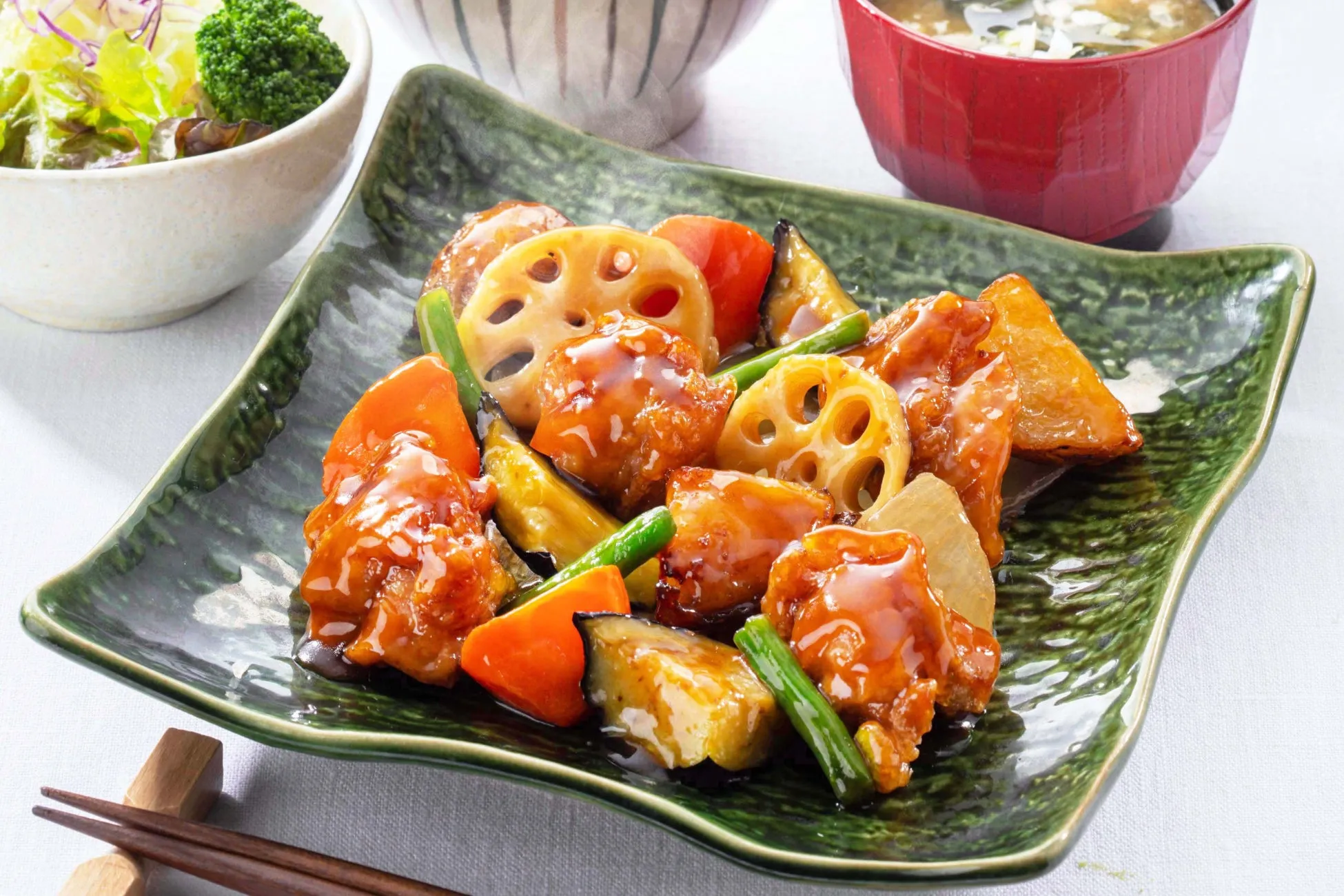 皿に盛られた中華料理の酢豚の俯瞰図。蓮根、人参、ナス、インゲン、揚げ物、ご飯、味噌汁、サラダなど、様々な食材が使われています。テーブルにはお箸が置かれ、料理が美味しそうに写っています。