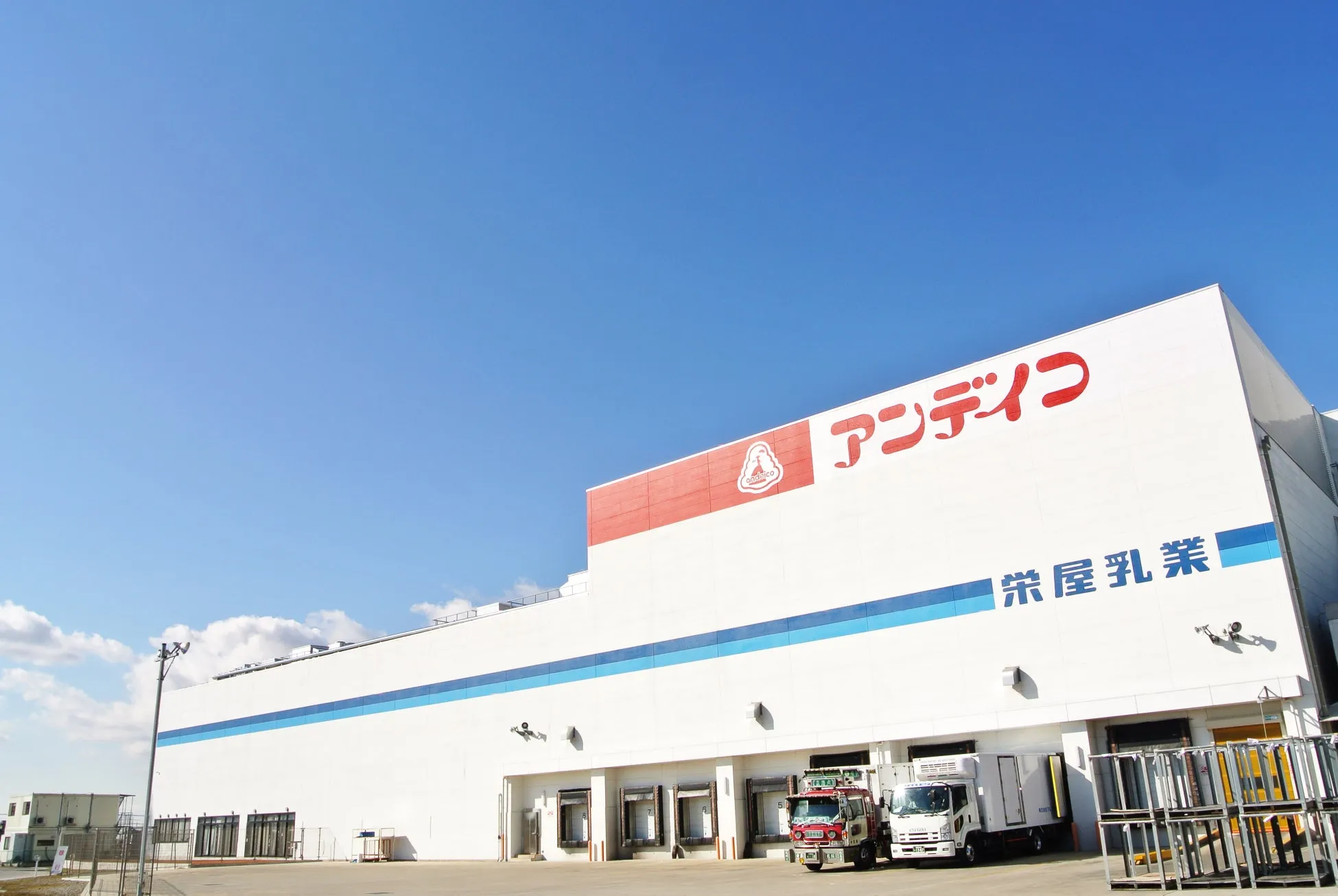 青空の下、白い建物に「アンデコ」と「栄屋乳業」の文字が記された写真。建物の前にはトラックが停まっている。