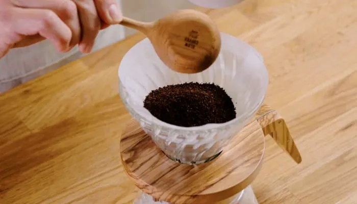 コーヒーを淹れる様子を写した写真。コーヒー豆を計量スプーンでフィルターに入れている。