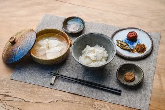 豆腐の入った器やごはん、佃煮の並ぶ朝食