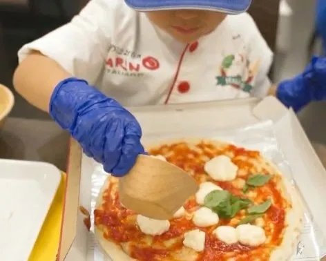 トマトソースを広げたピッツァ生地にチーズをのせる子ども