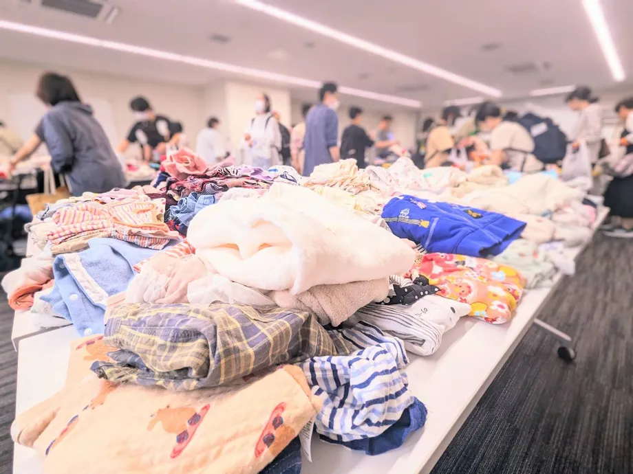 会場のテーブルに並べられた子ども服と参加者たち