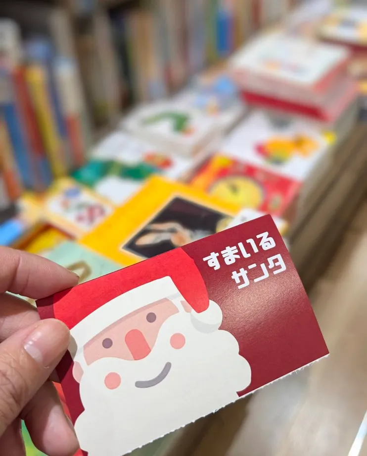 書店の本を背景に手に持った「すまいるサンタ」のカード