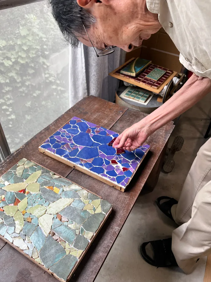 モザイク作品のそばで陶片を手に取る池田泰佑さん