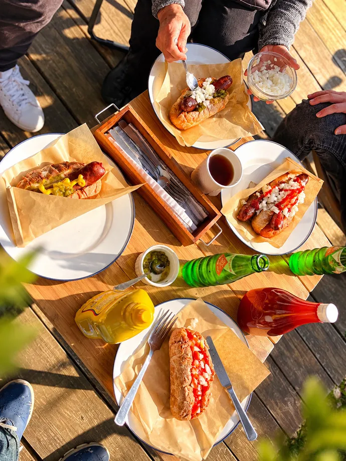 屋外のテーブルに並ぶ鹿肉ホットドッグと飲み物