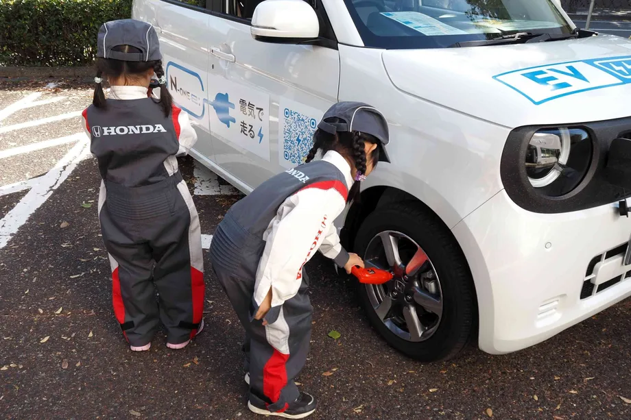 電気自動車のそばで制服を着る子どもたち