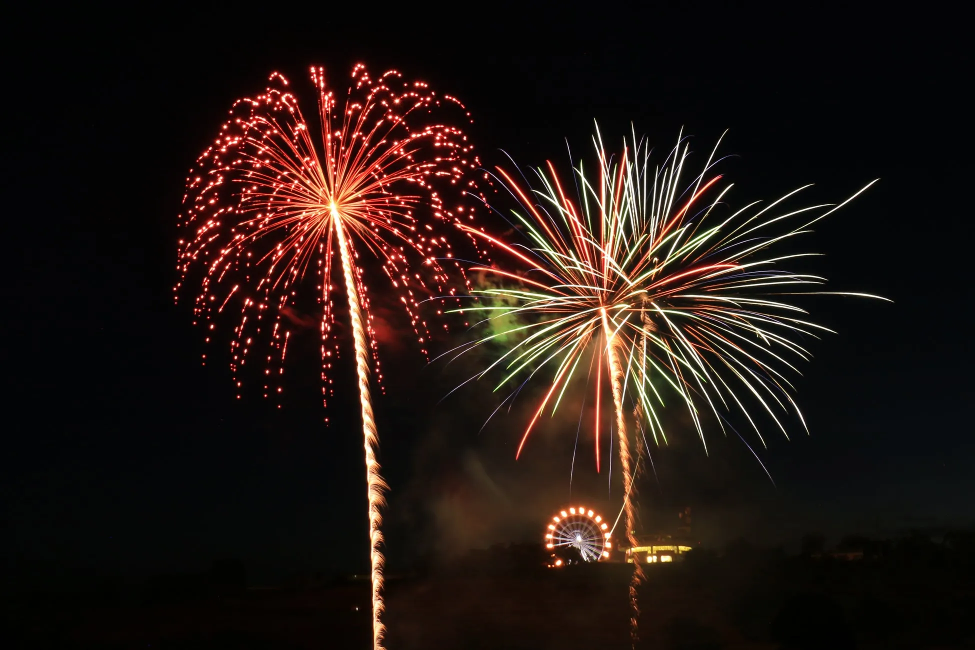 夜空を彩る花火とライトアップされた遊園地