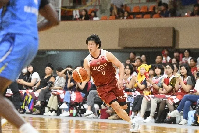 バスケットボールの試合で、ボールを持って走り、観客席にいる人々の前を走る男性バスケットボール選手。